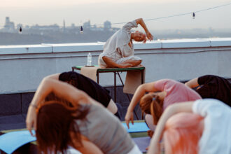 Grupa różnych ludzi ćwiczy jogę medytacyjną na dachu podczas pięknego zachodu słońca w letni wieczór