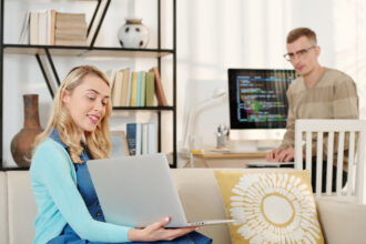 Dumna ładna młoda kobieta pokazuje mężowi ekran laptopa z wynikami swojej pracy
